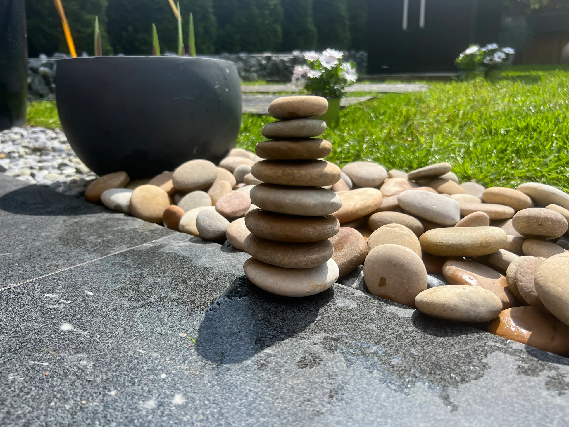 Stacked flat river pebbles forming a cairn on a granite slab beside a pebble border and lawn