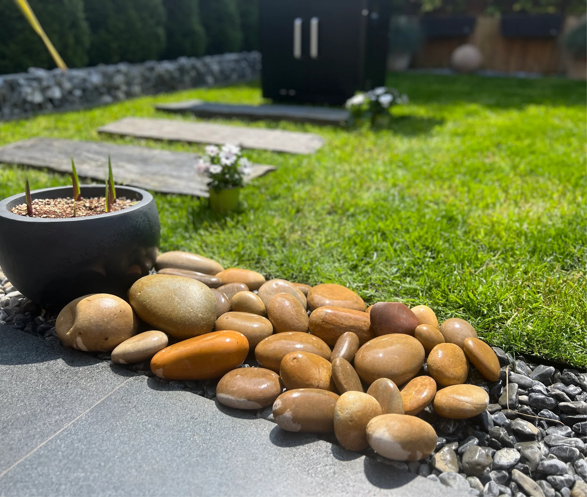 Polished ochre river pebbles edging a granite patio beside a lawn and planter